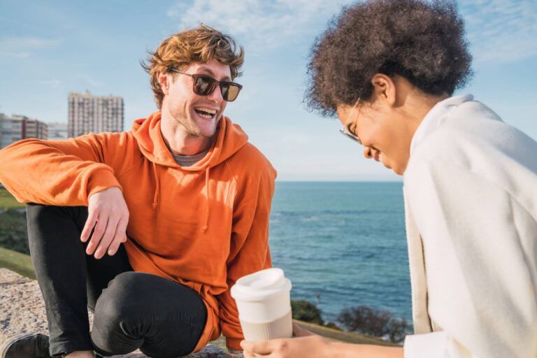 Portrait of two young friends spending good time together and having fun with the sea in the background.