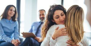 Young adult woman embracing and supporting friend during support group therapy session with diverse women