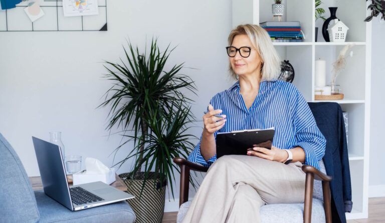 Professional Psychotherapy online. Middle aged female Psychologist having video call consultation on laptop while sitting on armchair