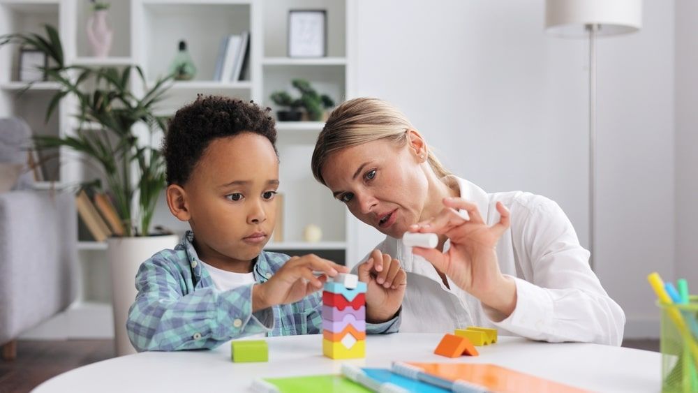 Professional psychologist observes small multiracial boy playing with puzzle game, assessing his readiness for preschool.