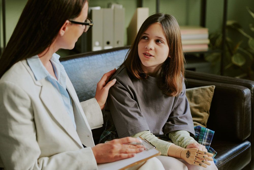 Teenage girl with prosthetic limb engaging with therapist on sofa focusing on recovery and future steps