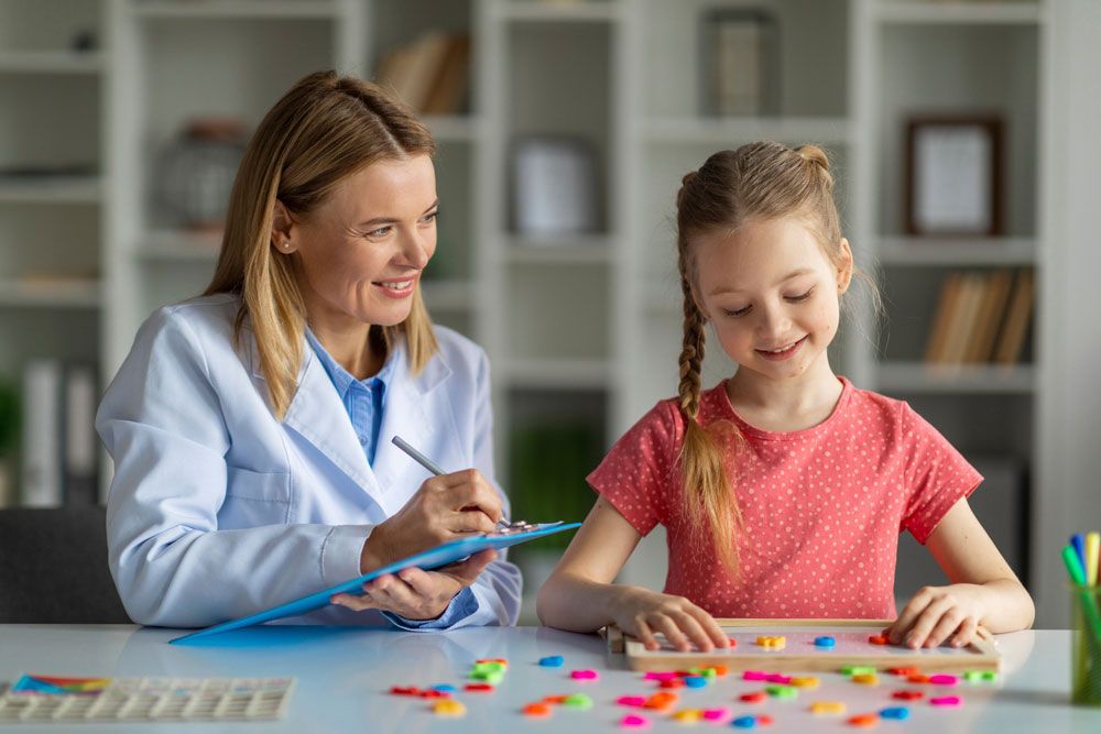 Woman psychologist watching little girl playing with logical game, evaluating readiness for elementary school