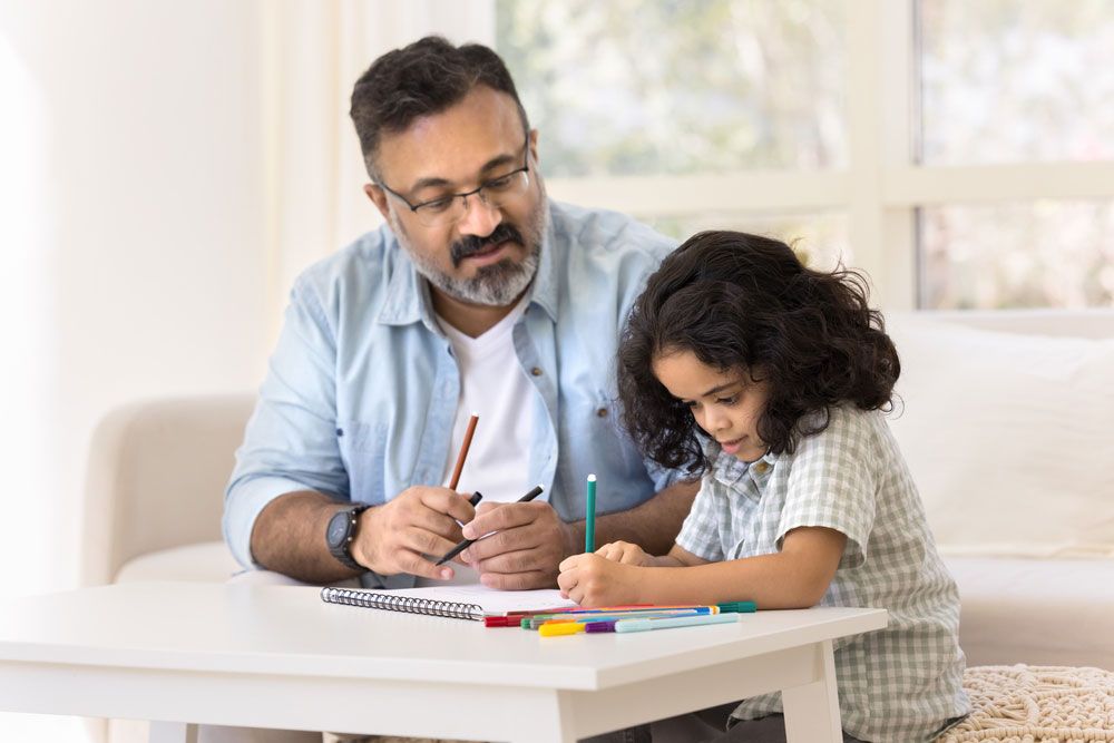 Focused Indian grandfather and cute granddaughter kid drawing creative colorful doodles in paper album together