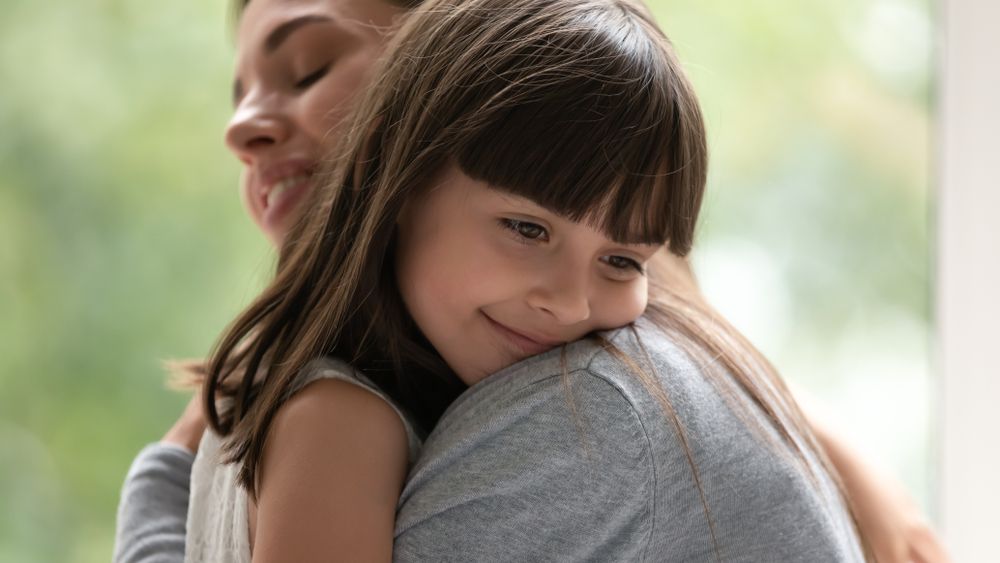 Side view close up head shot happy little adopted kid girl put head on mothers shoulder