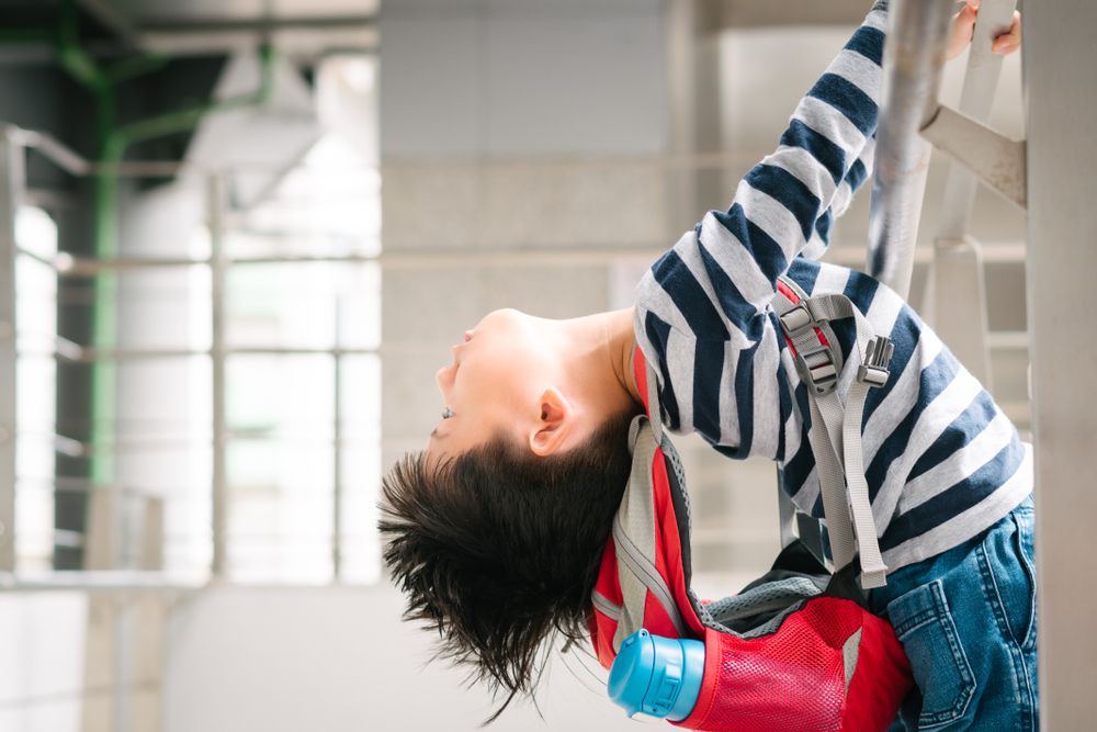 Little Asian hyperactive difficult boy hold handrail and lean body and head backwards