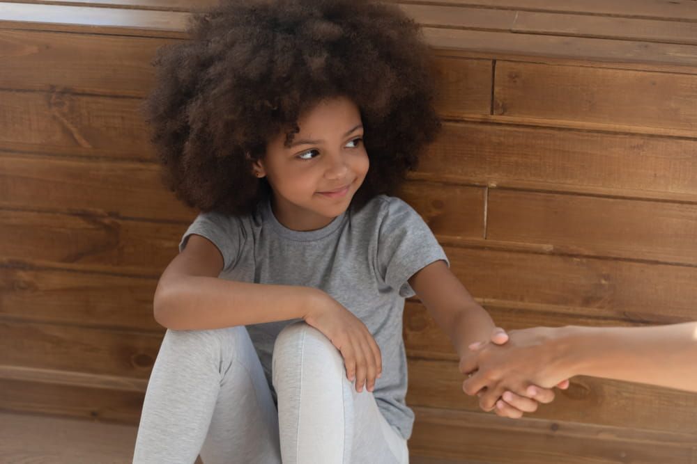 Happy cute small kid girl orphan holding hand of foster care mom sit on floo