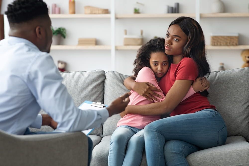 Black woman hugging her scared daughter while attending child psychologist