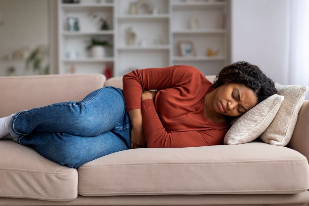 Young black woman clutching her abdomen in discomfort at home