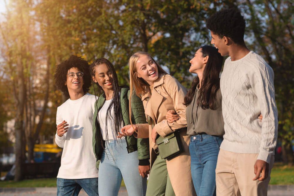 International group of cheerful teenagers laughing while walking by golden park