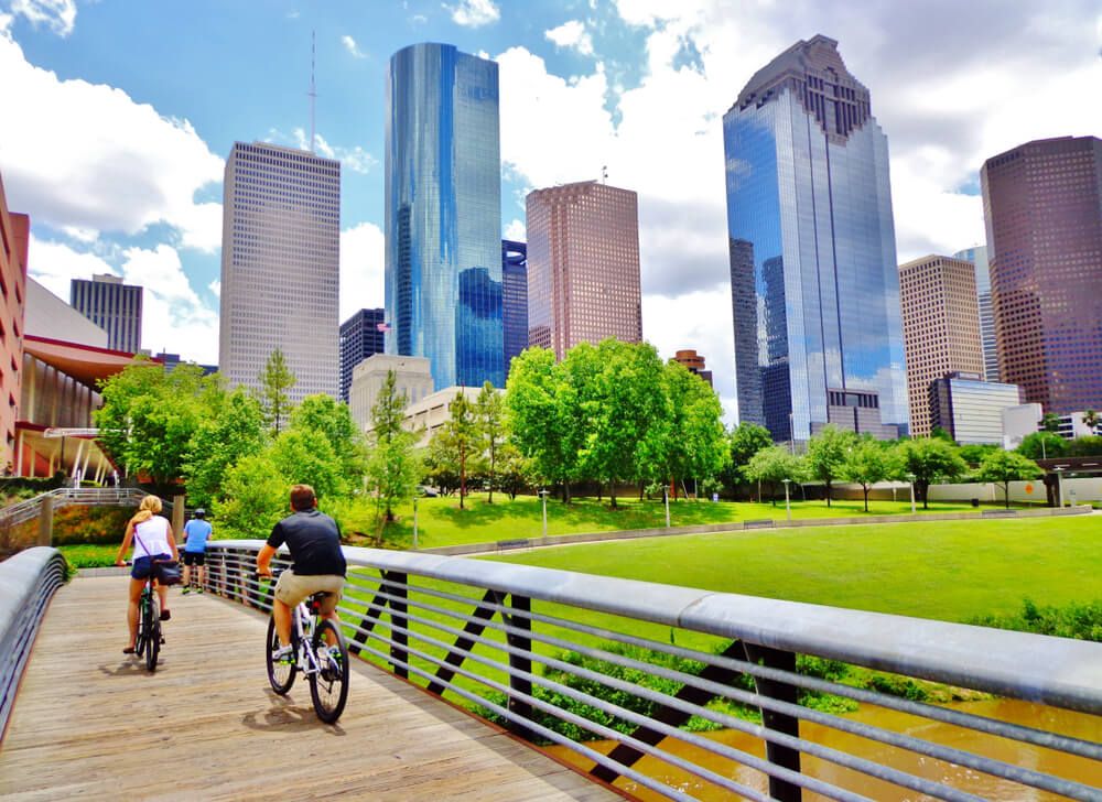 Bicyclists cross wooden bridge in Buffalo Bayou Park, with a beautiful view of downtown