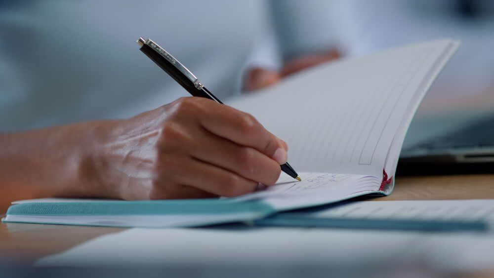 Closeup mixed race businesswoman hands making notes in notebook at workplace.