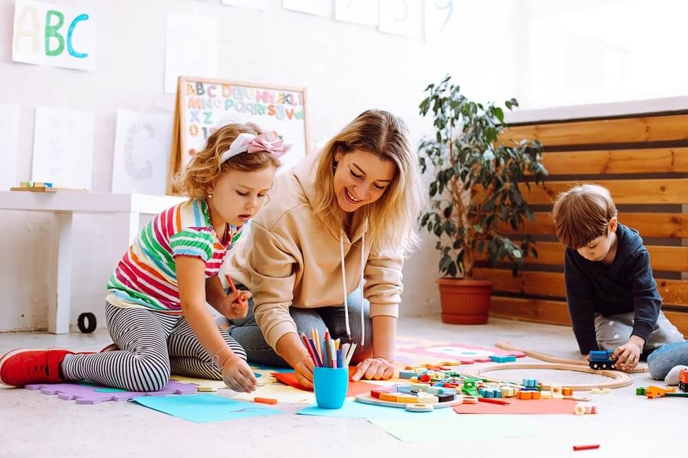 Smiling female psychologist play and test children, make crafts, handmade toys and arts in kid development center for pre schoolers.