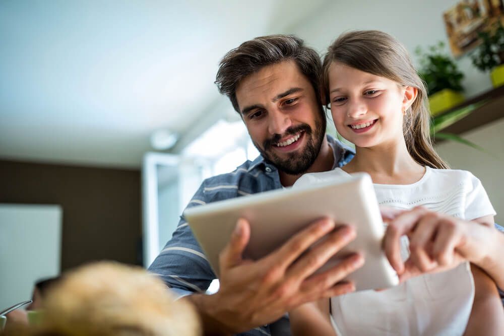 Father and daughter using digital tablet in the living room at home