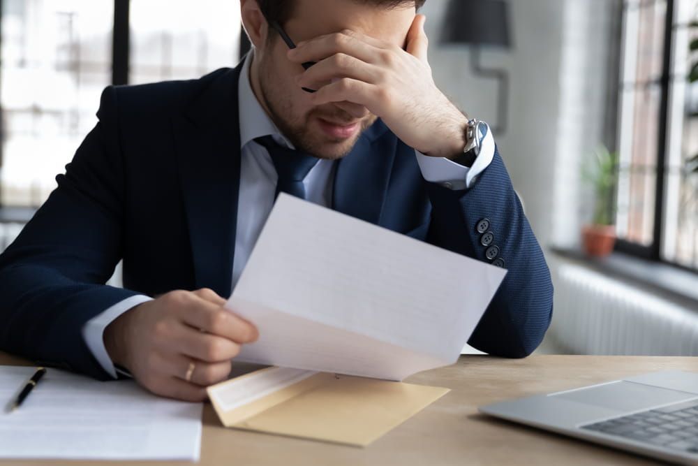 Upset male employer or boss sit at desk feel distressed disappointed reading post paper correspondence,