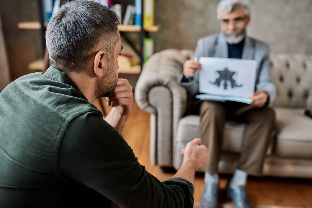 Rear view of caucasian man passing Rorschach test sitting on sofa during appointment with psychotherapist in office, selective focus. Psychotherapy concept