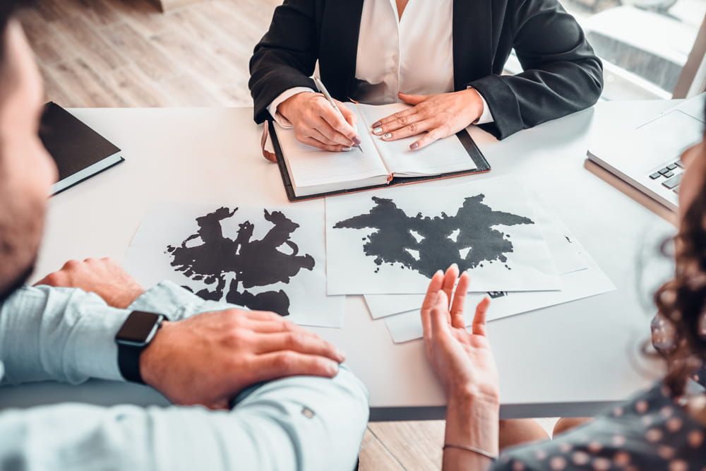 Cropped image of family sitting on psychology consultation on the desk, passing rorschach test with help of female psychotherapy specialist.