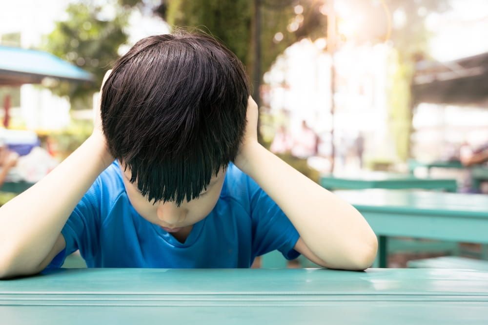 Close up of Asian autistic student child sit at table at school cover ears with hand and close eyes due to stress and anxiety.