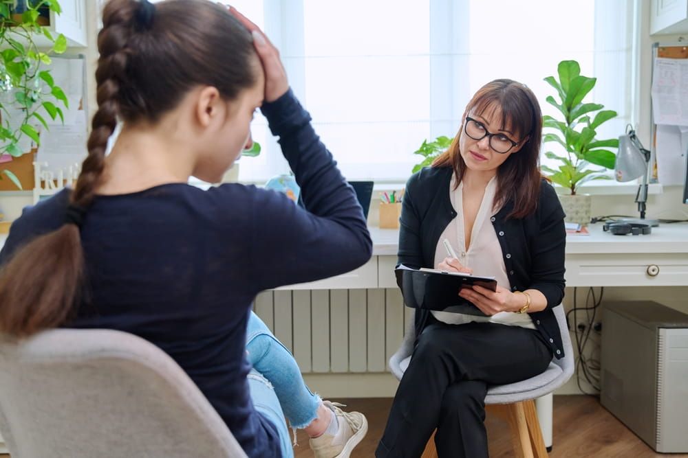 Teenage girl high school student talking with mentor, psychologist in office