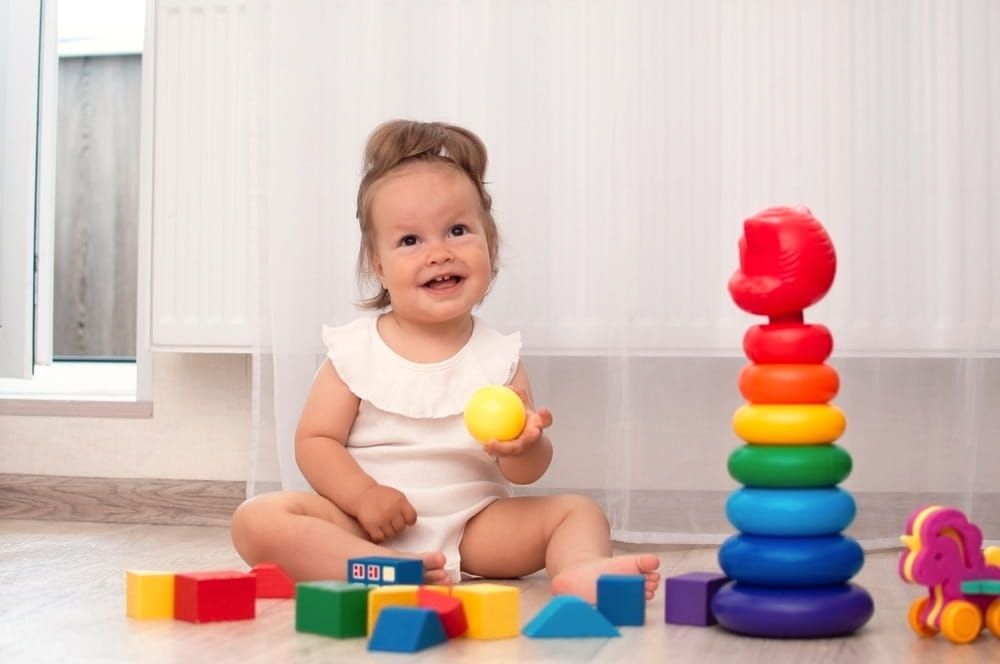 Charming kid is playing at home on floor with colorful cubes. Children's educational wooden toys.