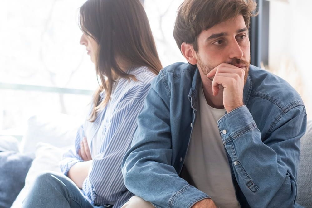 A young couple sitting in silence on the couch, facing emotional distance and relationship struggles.