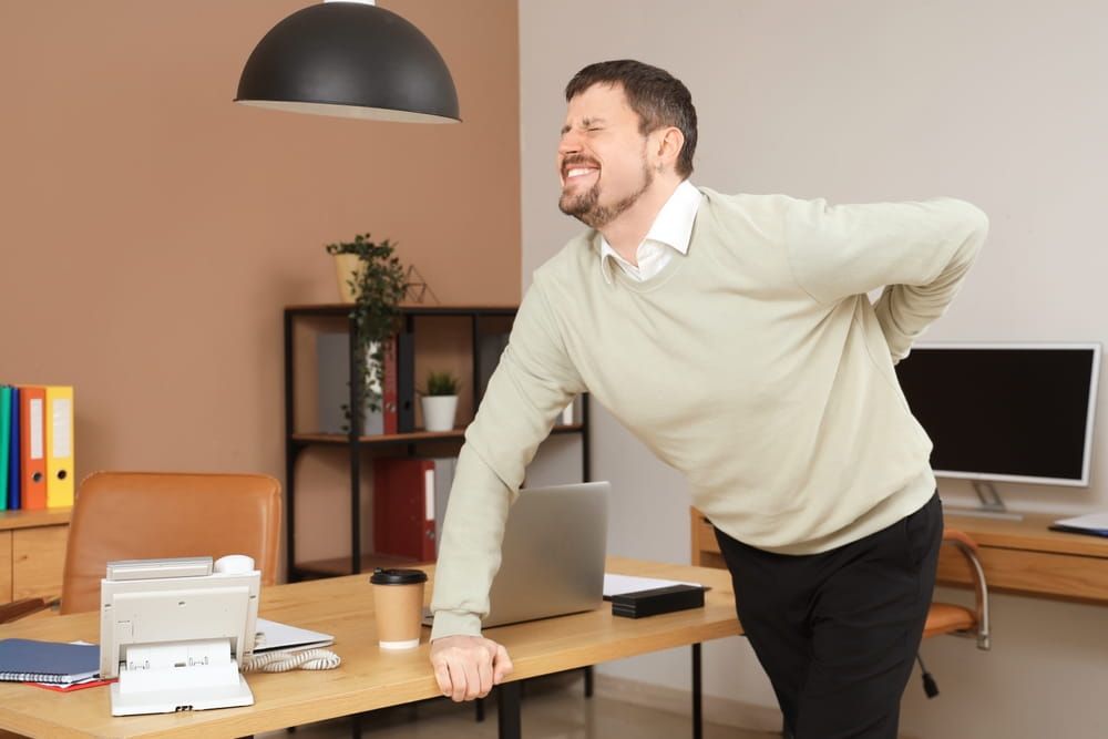 Young man suffering from back pain near table in office