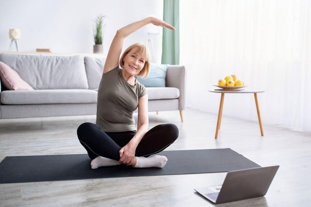 Athletic senior woman doing yoga in front of laptop during home workout