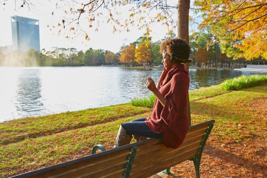 Woman listening music in the autumn park at sunset with headphones