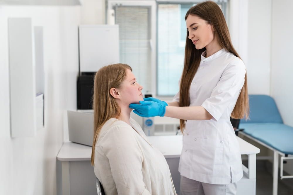 An endocrinologist wearing rubber gloves palpates the lymph nodes and thyroid gland of a patient with excess weight and acne.