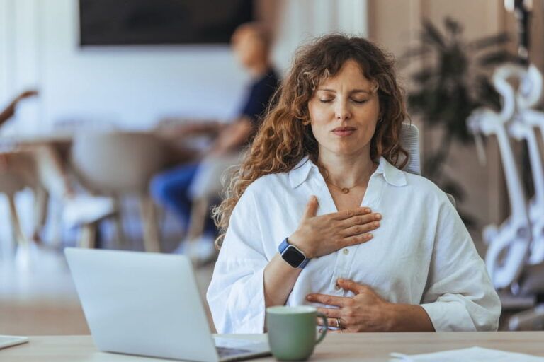 A woman performs calming mindfulness meditation at her workspace, emphasizing wellness and stress management in a work environment.