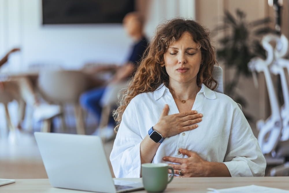 A woman performs calming mindfulness meditation at her workspace, emphasizing wellness and stress management in a work environment.