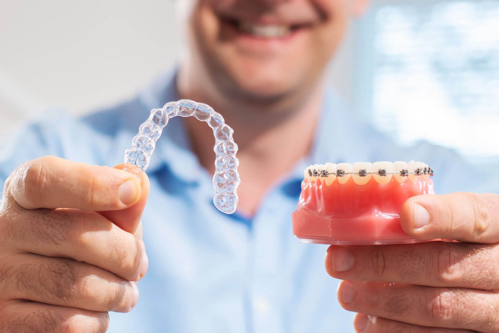 Smiling dentist holding aligners and braces in hand