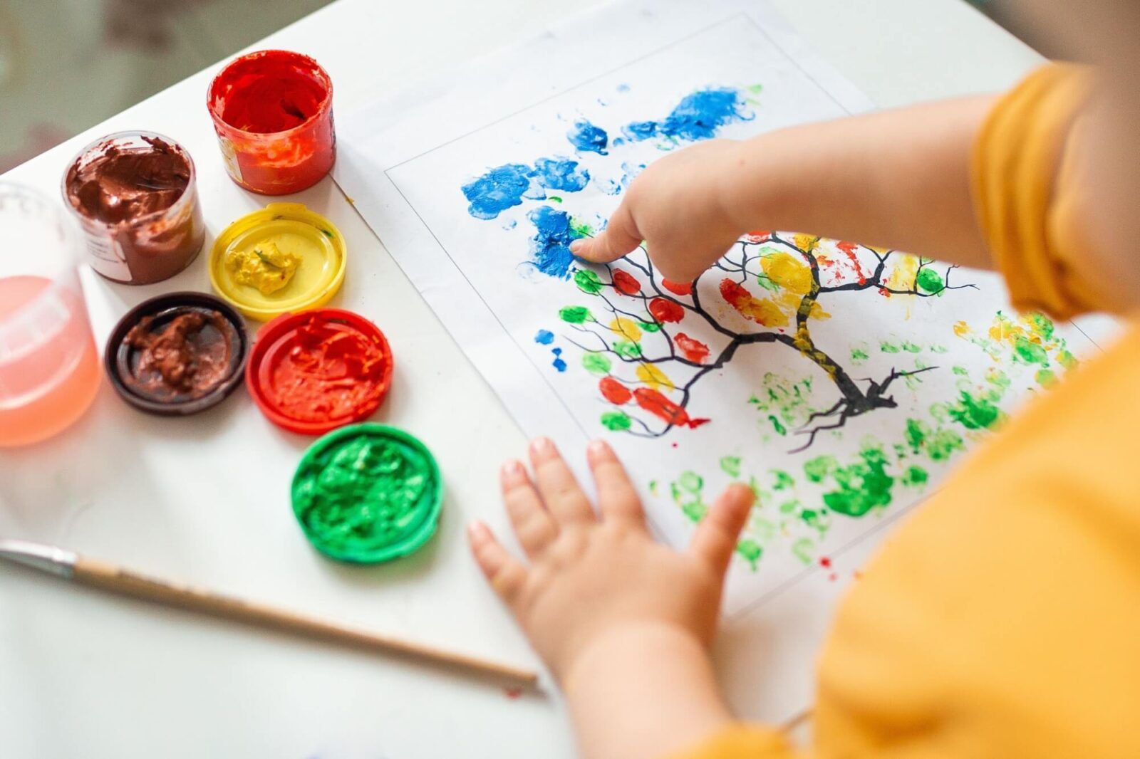 A child draws leafs on a tree. Ideas for drawing with finger paints. Finger painting for kids on white background