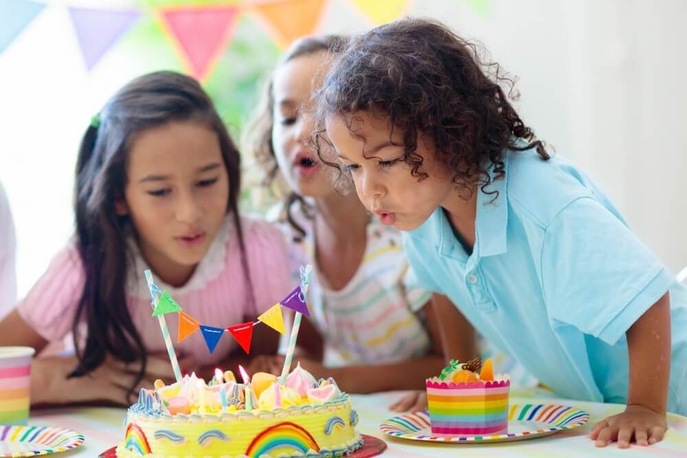 Little curly boy blowing candles and opening birthday presents.