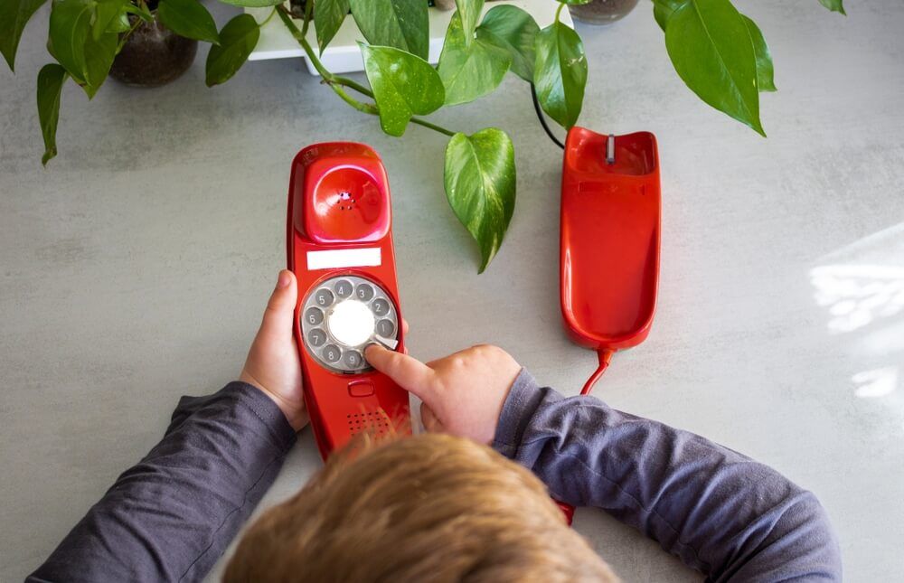 child's hands and hair using an antique red phone at home