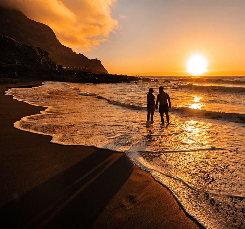 A couple in love stands in the ocean in the evening looking at the beautiful sunset on the island of Tenerife.Spain.