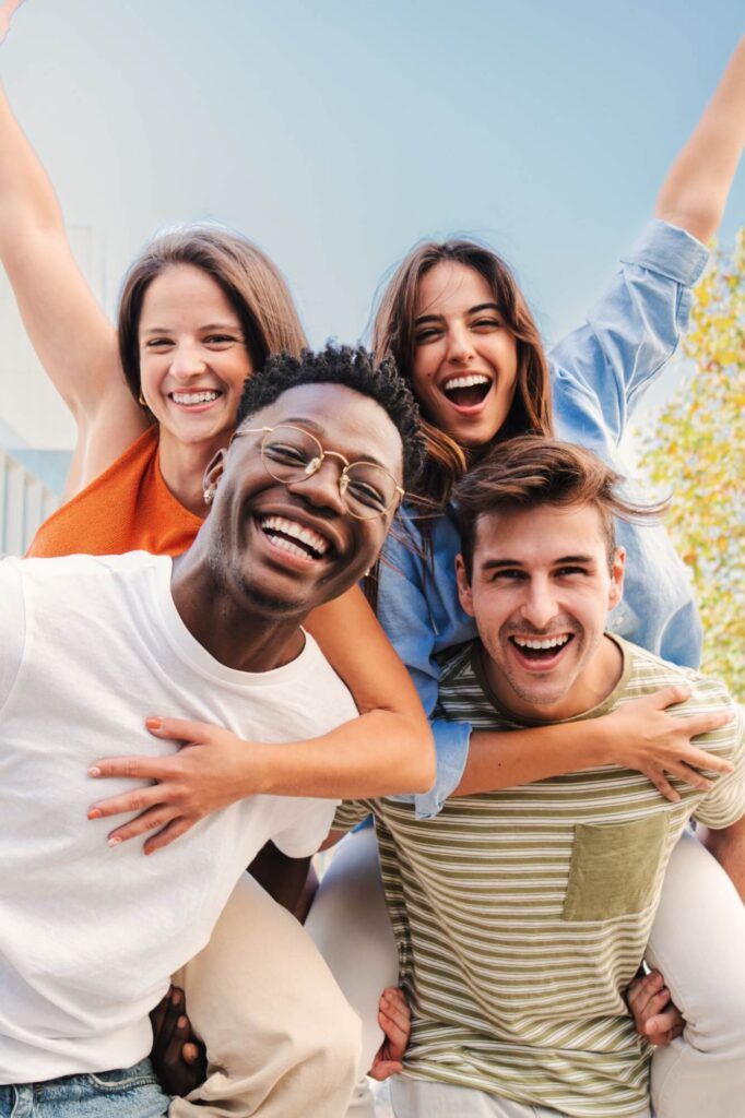 Vertical portrait of two multiracial young friends giving piggyback ride to his girlfriends.