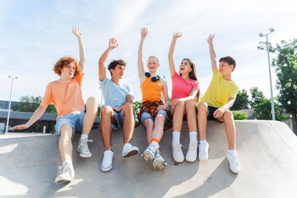 Portrait of smiling teenagers, children wearing stylish casual clothes, colorful t shirts raising hands on urban street