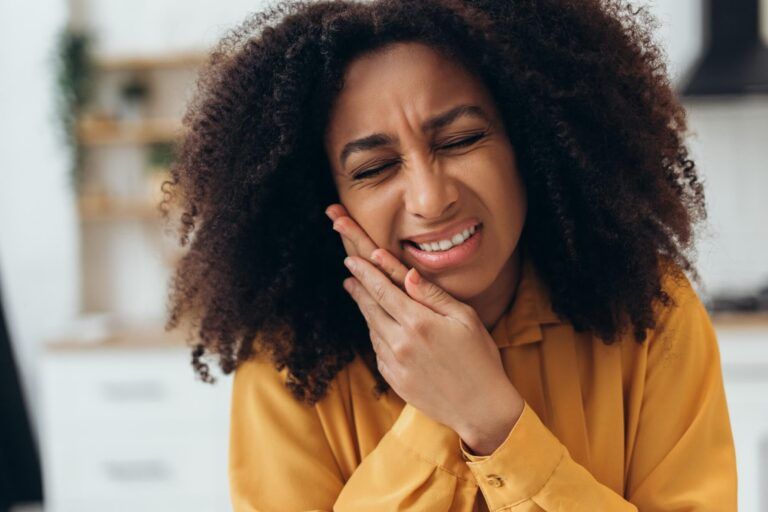 Young African American woman suffering from strong toothache touching her cheek