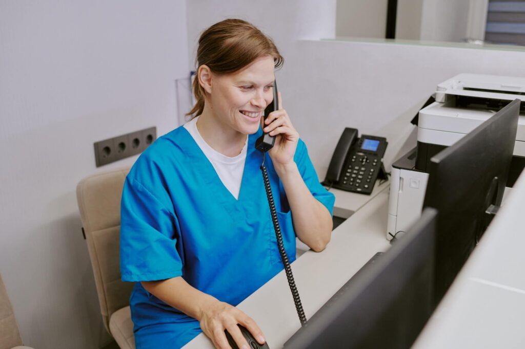 adult woman sitting at reception desk talking on phone while looking at computer monitor