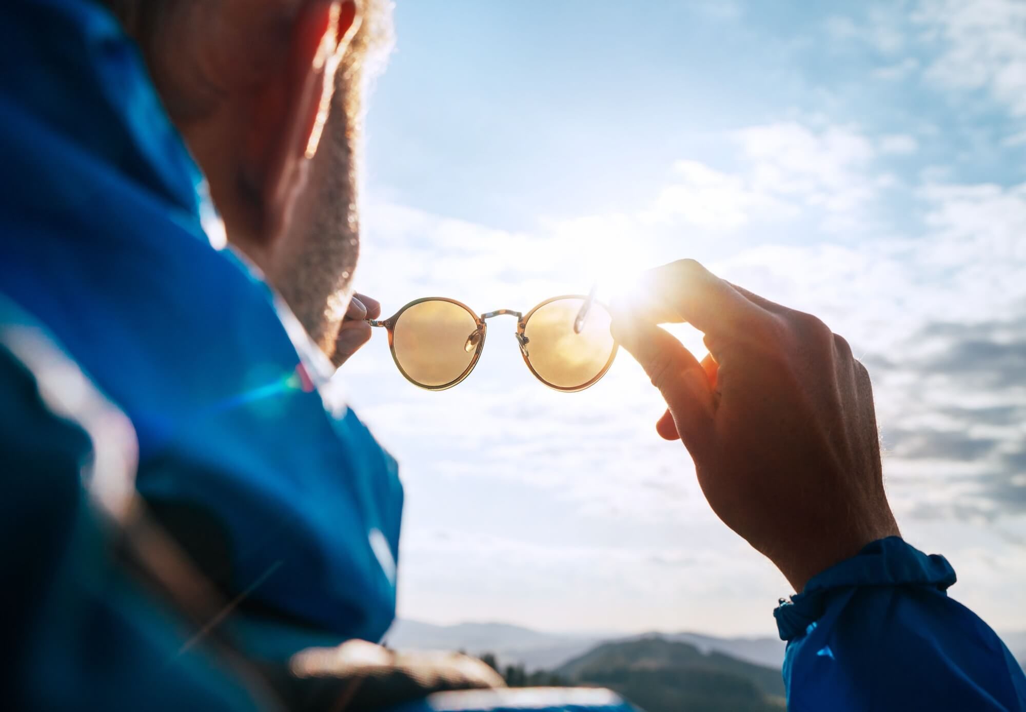 Backpacker man looking at bright sun through polarized sunglasses enjoying mountain landscape.