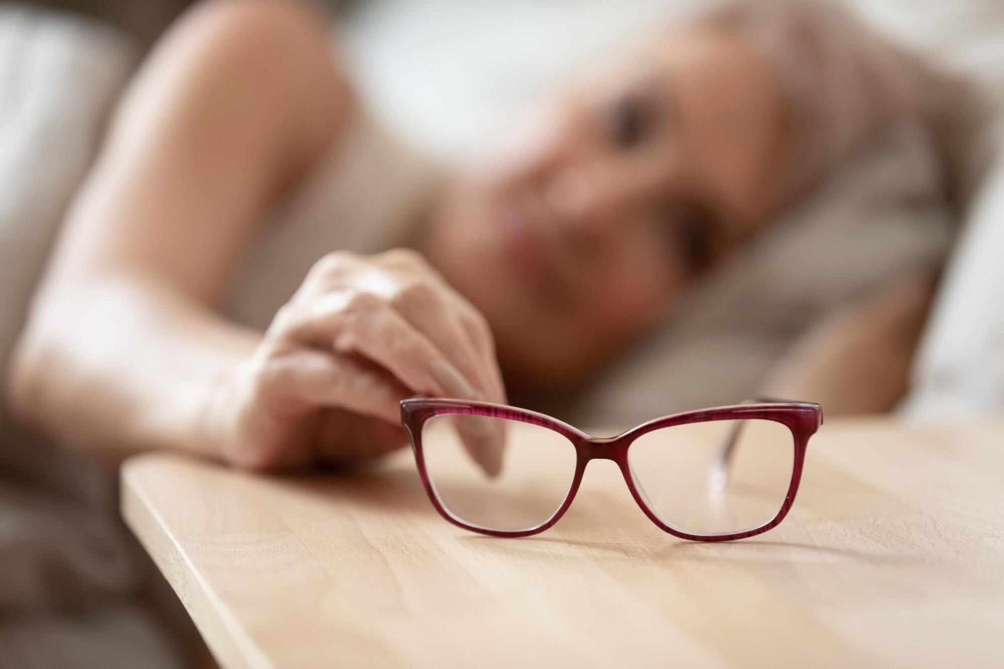 woman holding taking optical glasses from bedside table waking up in morning