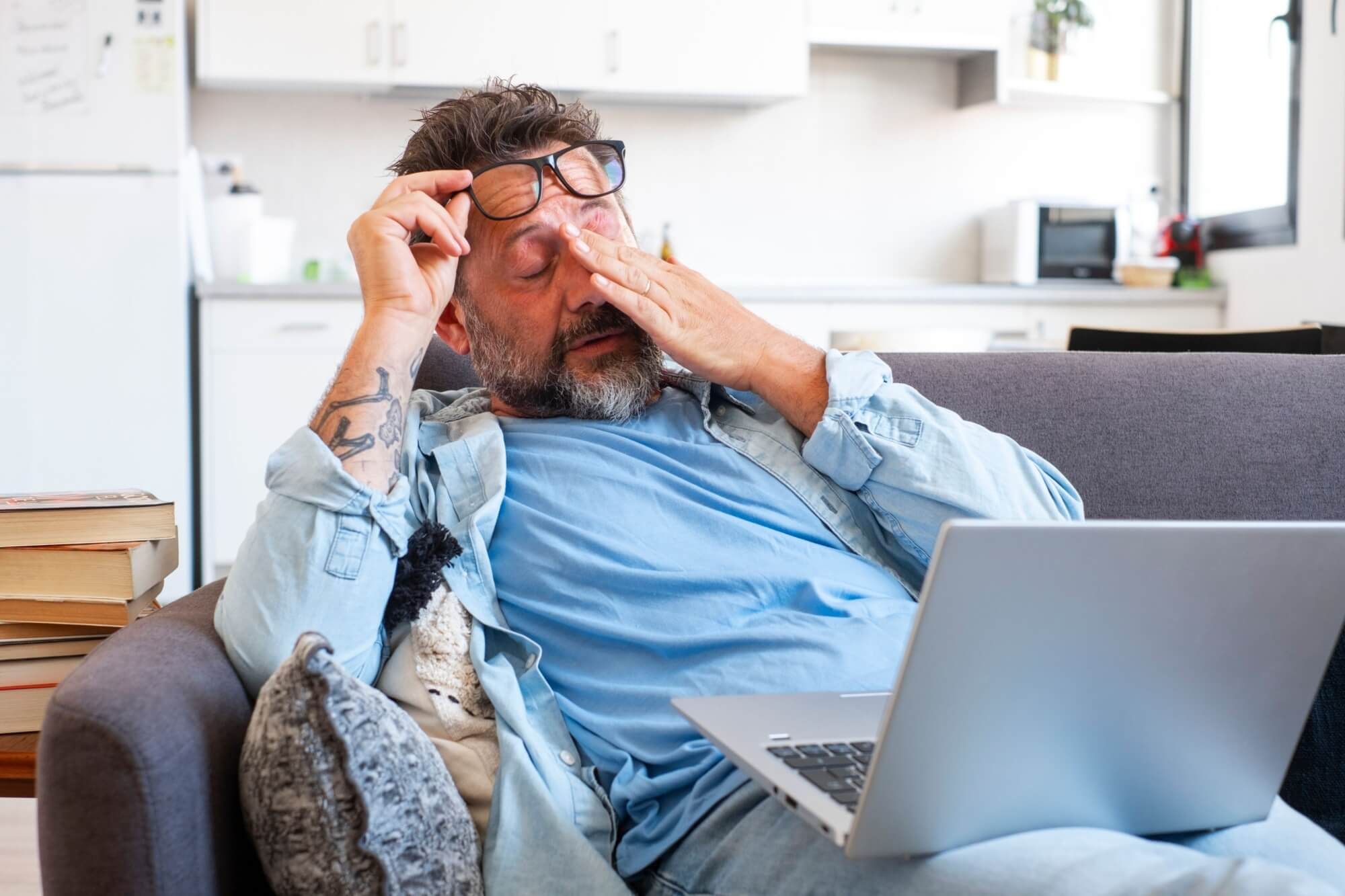 Tired businessman takes off glasses and feels eye strain from working online with laptop,