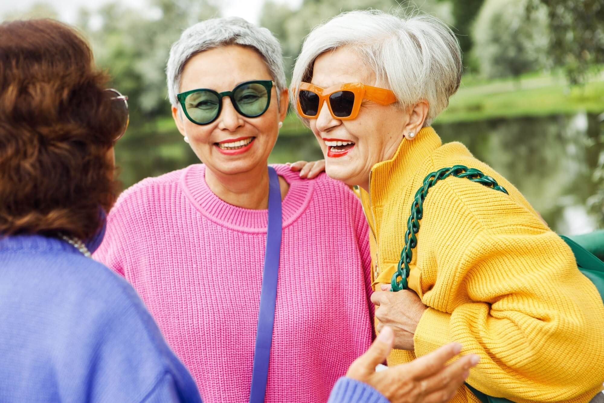Pensioner female friends meet in the park, chatting and laughing merrily. Friendship, people and golden age concept.