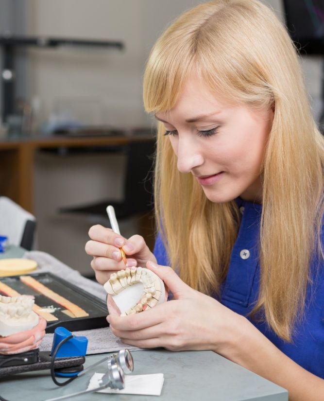 Dental lab technician applying porcelain to dentition mold in a lab
