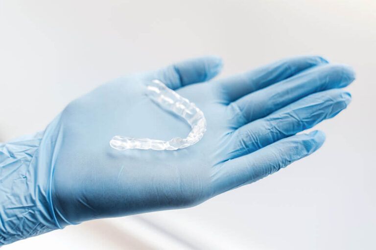 Dentist doctor in latex gloves holding orthodontic aligners, selective focus on hand.