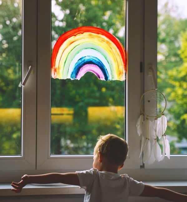 Сhild boy on background of painting rainbow on window.
