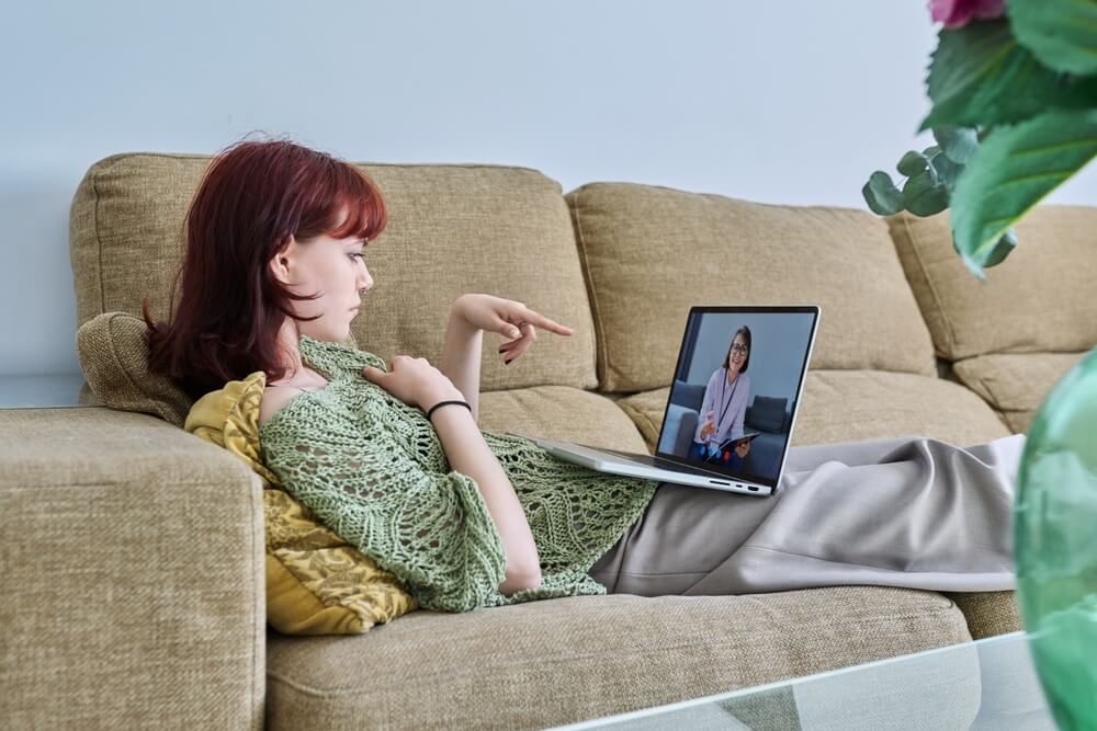 Online therapy, young female lying at home having video conference with psychologist