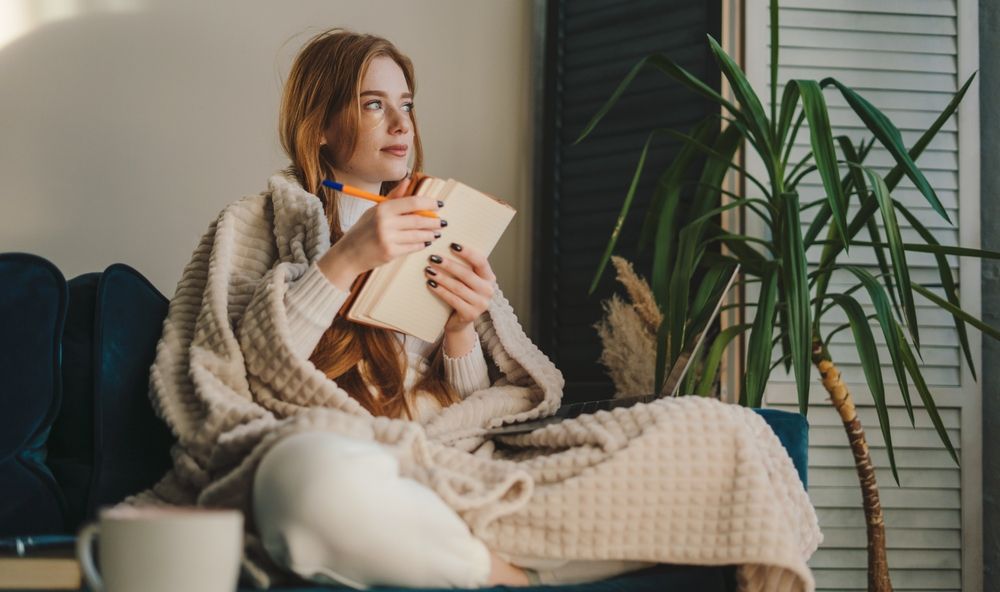 Thoughtful and cozy redhaired woman sitting with her legs crossed and taking notes