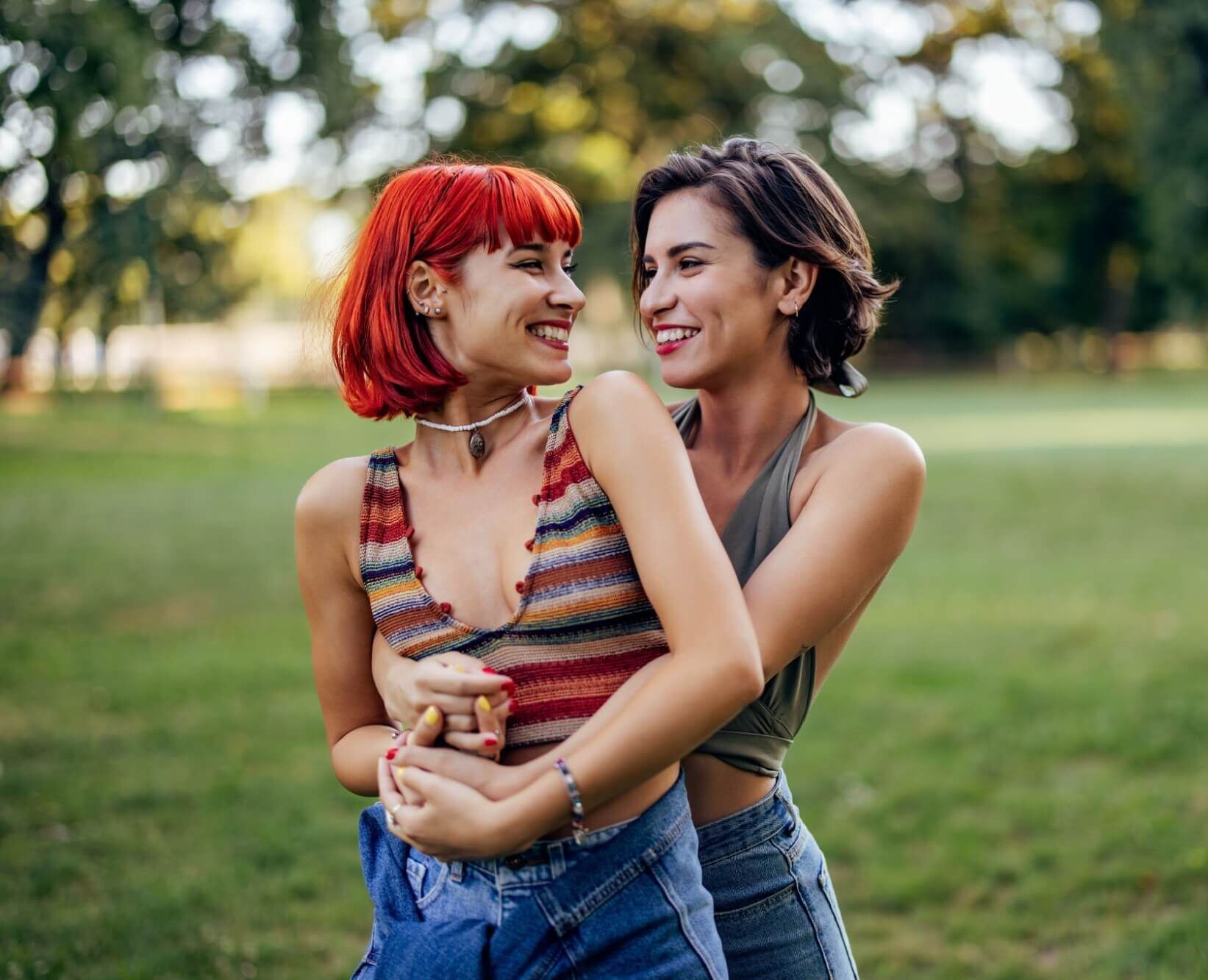 Girls in a park, lgbt couple in a hug, looking and smiling at each other.