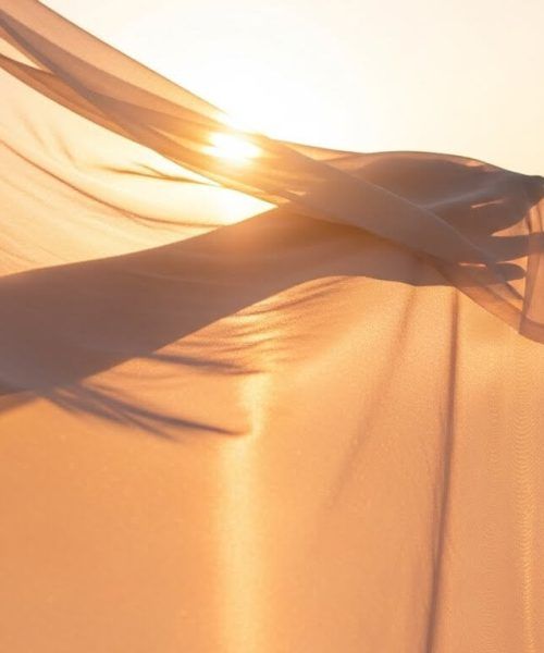 delicate, light-colored fabric billowing gracefully, capturing the warmth and glow of the golden hour sun